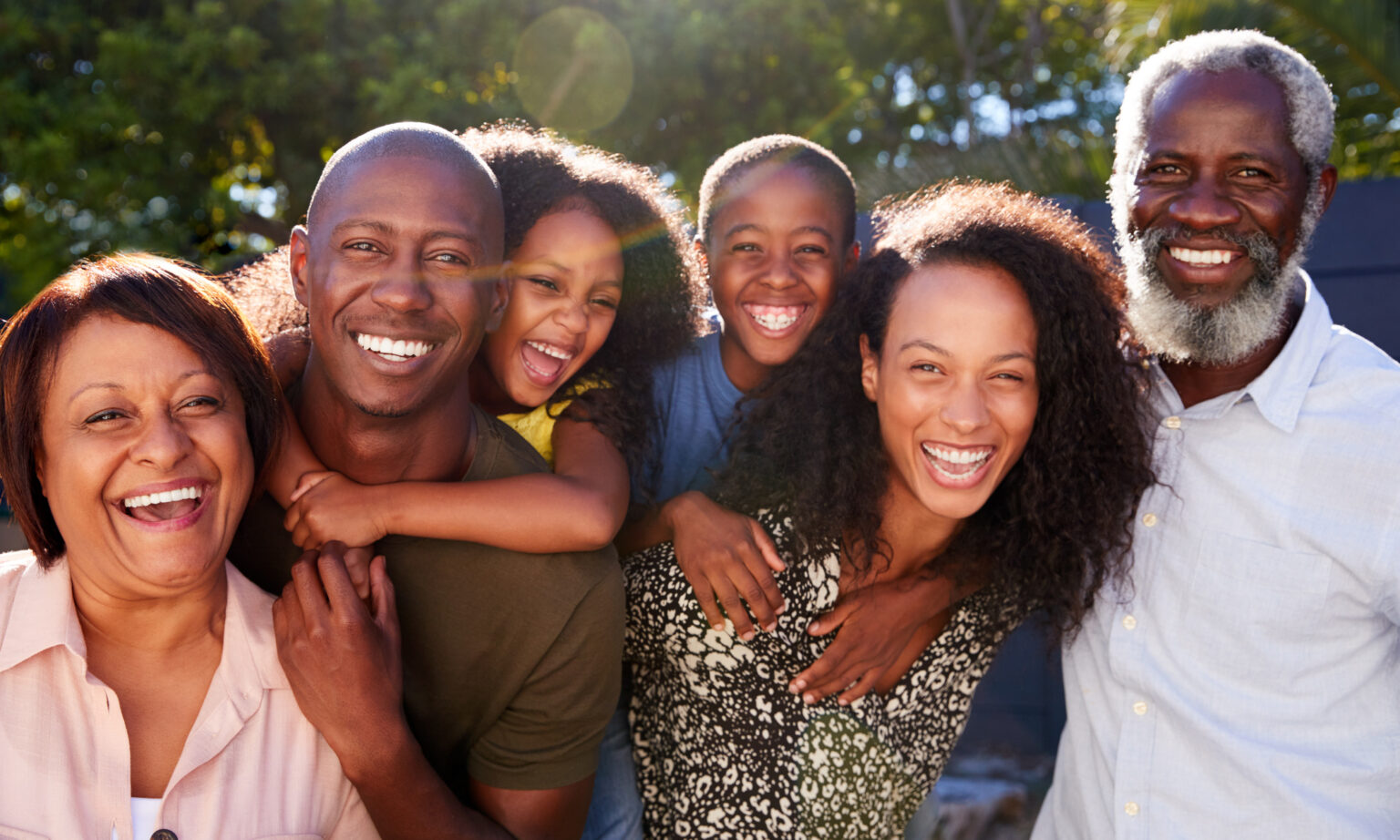Outdoor Portrait Of Multi-Generation Family In Garden At Home Against Flaring Sun