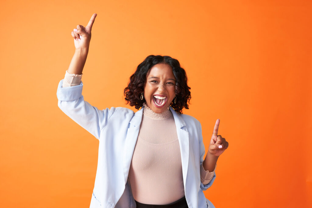 Excited woman in a white blazer cheering and pointing to the sky with both hands