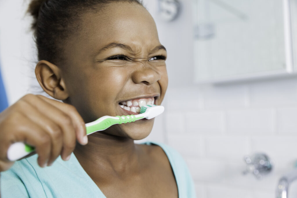 Little girl grins while brushing her teeth