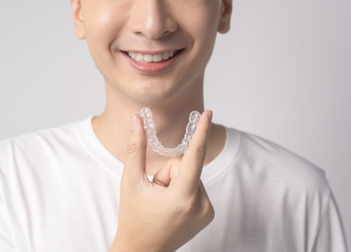 Close up of a young man smiling and holding his Invisalign aligner between his thumb and forefinger