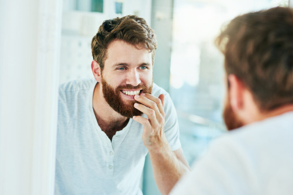 Handsome man with full beard examining his smile in the mirror