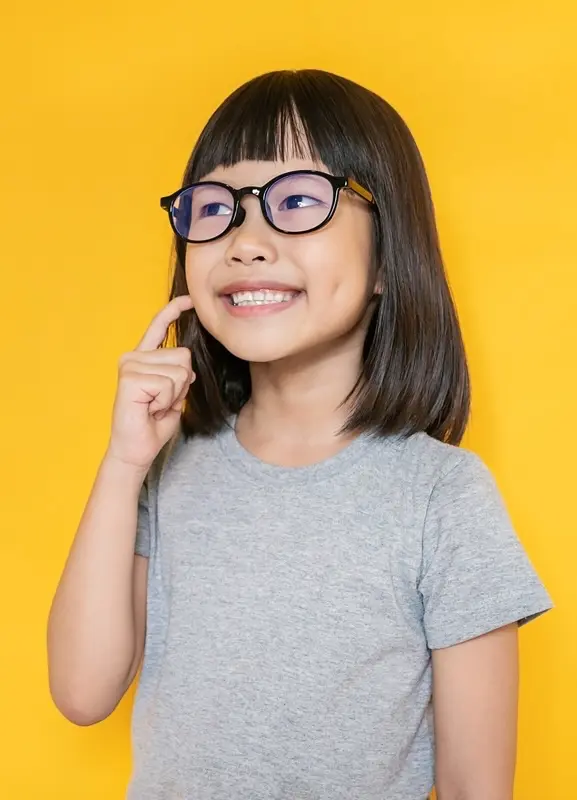 Happy child with glasses smiling brightly and pointing to her teeth, showing excitement about early orthodontic care at Labbe Family Orthodontics.