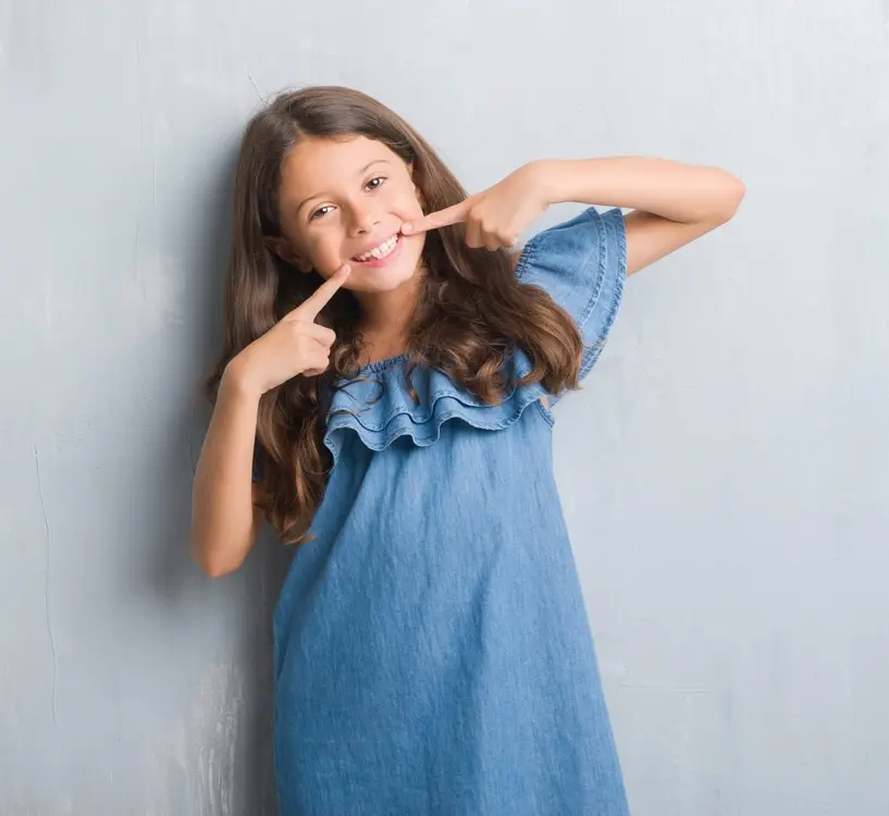 Smiling young girl pointing to her teeth, showcasing confidence after early orthodontic treatment at Labbe Family Orthodontics.